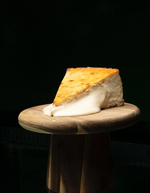 Porción individual de tarta de queso artesanal de Queso 7, sobre tabla de madera con fondo oscuro